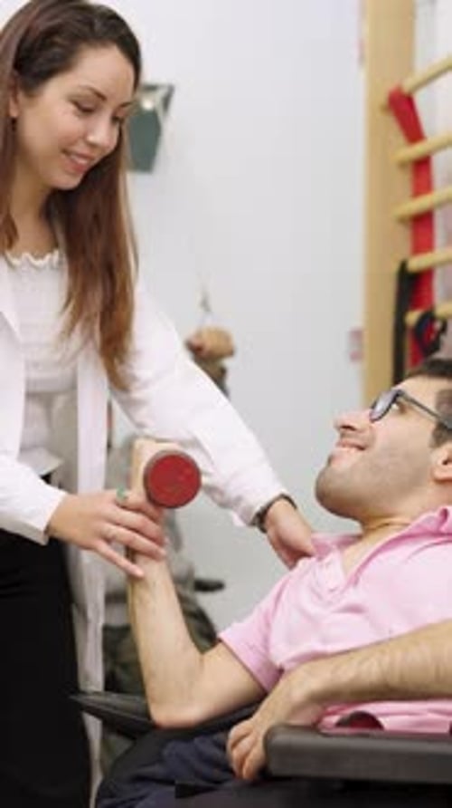 Woman helping man lift weight in rehabilitation center