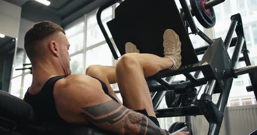 A Muscular Man Performs Exercises on a Sports Training Apparatus for Leg Muscles in a Gym Lifting