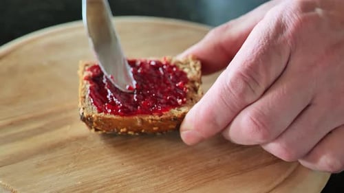 Toast with jam. hands spread jam on bread on the kitchen table.