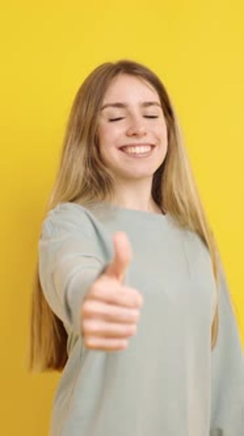 Smiling Woman Giving Thumbs Up on Yellow Background