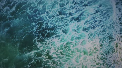 Aerial drone shot capturing a mesmerizing view of waves gently washing up onto the shore,