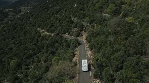 Large white motorhome is driven along a narrow road in the countryside