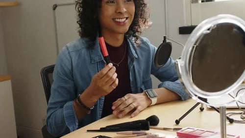 Creador no binario que muestra un tono de brillo de labios rojo antes de hacer una demostración del consejo de uso de la brocha en polvo en un estudio doméstico