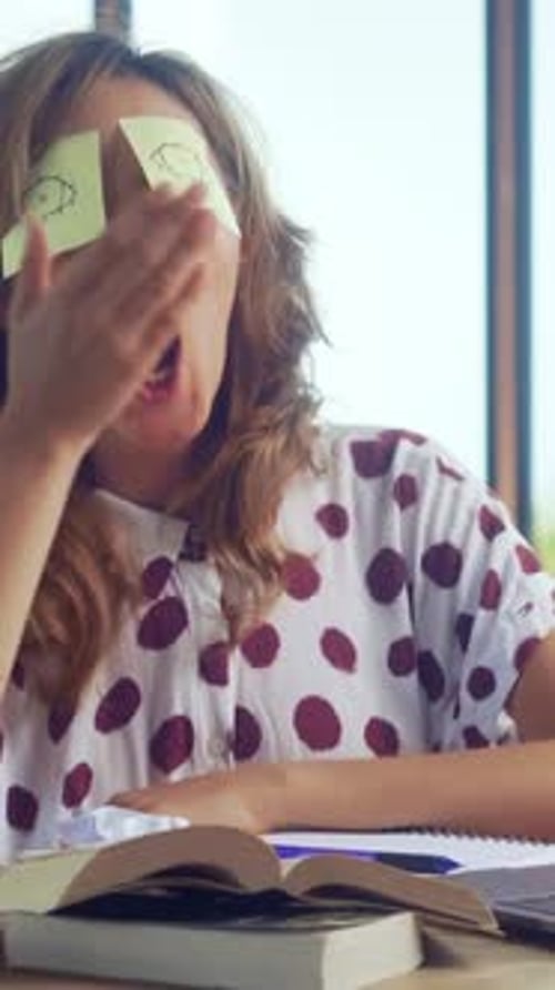 Woman Engages in Playful Study Break With Sticky Notes on Eyes