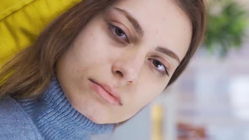 Vertical Video of Thoughtful young woman resting on sofa at home looking at camera.