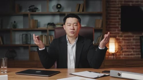 Relaxed Asian Employee Meditating at Office Desktop