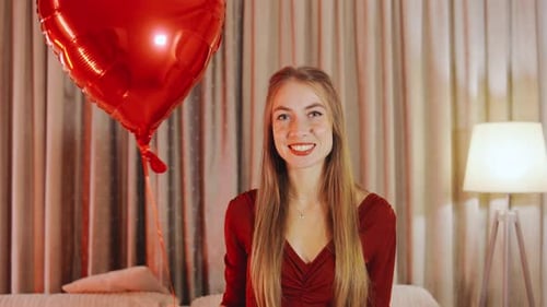 Smiling Woman Holds Heart Balloon in Living Room