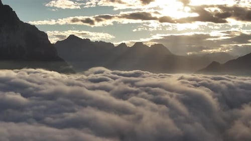 Mountain peaks rise above a sea of clouds at sunrise with warm light illuminating the mist