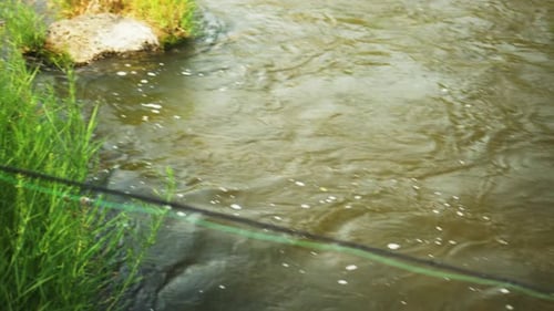 Detailed shot of a man fly fishing on a river on a sunny day in fast-moving waters.