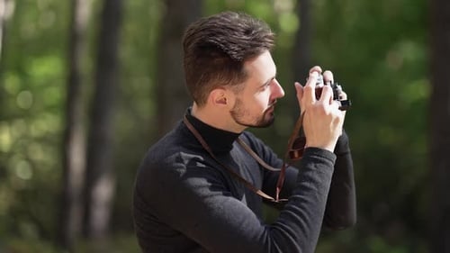 Side View Portrait of Smiling Caucasian Young Man Taking Photos of Nature with Camera Standing in