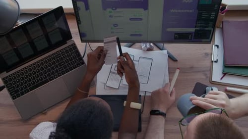 Black Female UX Designer Discussing Mobile App Plan on Paper with Man at Desk