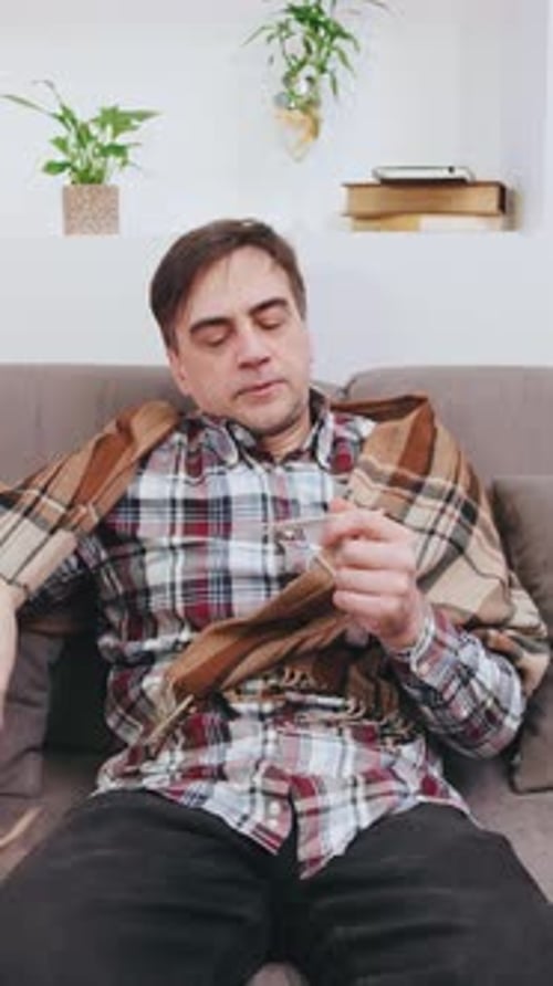Vertical Video Grayhaired Elderly Man in a Plaid Shirt and Scarf Measures His Body Temperature