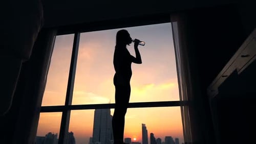 Silhouette Woman Drinking Water at Sunset in City