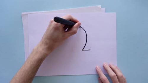 Hands drawing Libra zodiac sign on sheet of paper. Top view.
