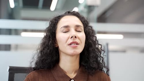 Young businesswoman relaxing breathing deeply while sitting at a workplace in a business office.