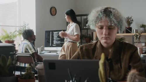 Female Programmer Working on Laptop while Colleagues Chatting in Office