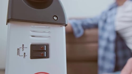 A man turns on a heater to warm up in a cold room, using it during an energy shortage.
