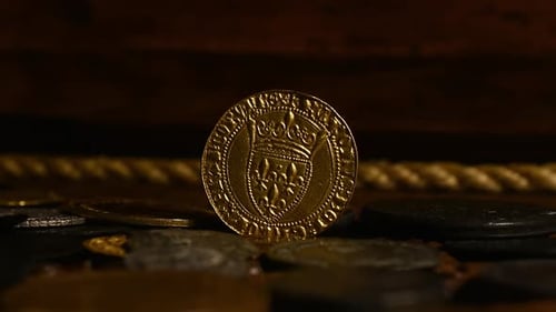 French medieval gold coin in a chest with other coins in rotation.
