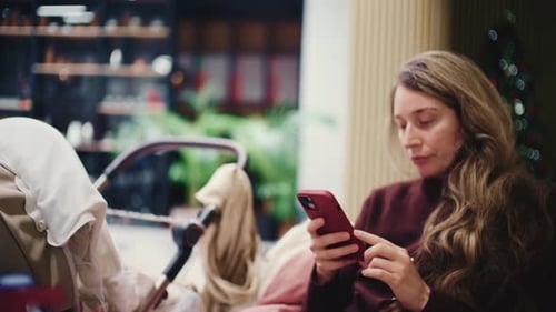 Woman sitting comfortably indoors while using her smartphone next to a baby stroller