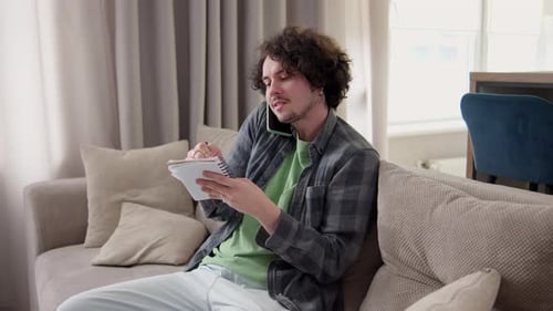 Man on Phone Writing in Notepad at Home