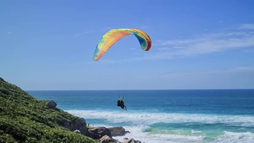Gleitschirmflugszene vor dem Strand mit Felsen, Bergen und Sand mit Leuten, die Spaß haben
