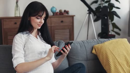 Pregnant Woman Using Smartphone on Couch at Home