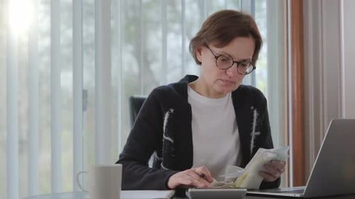 Woman Checking Bills Taxes Bank Account Balance and Calculating Expenses in the Living Room at Home