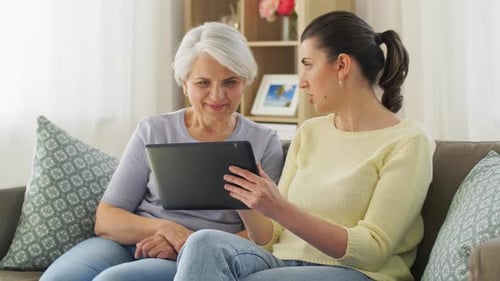 Senior Woman and Adult Daughter Use Tablet at Home