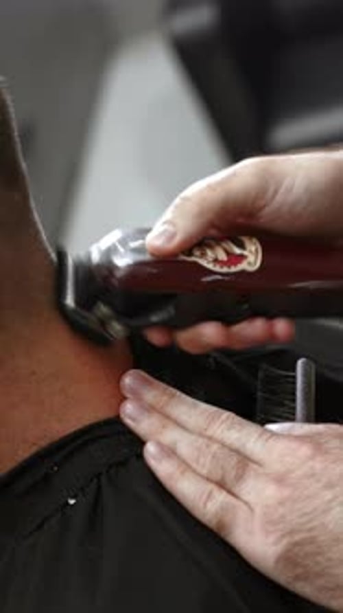 Professioneller Friseur, der eine elektrische Haarschneidemaschine am Halsclip des Kunden verwendet