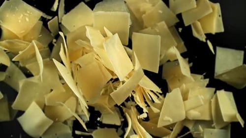 Las hojuelas de queso parmesano vuelan hacia arriba sobre un fondo negro filmadas con una cámara de alta velocidad a 1000 fps