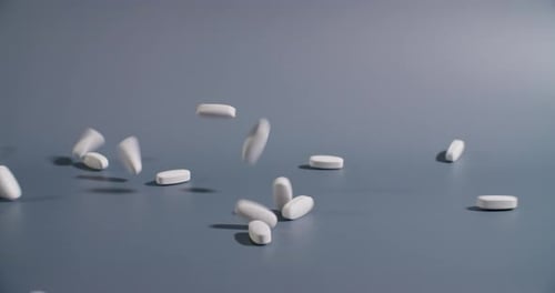 Close-up of a handful of white pills falling onto a gray background in slow motion.