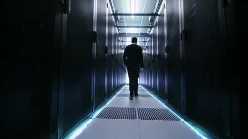 Foto siguiente de un ingeniero de TI recorriendo el pasillo del centro de datos con filas de servidores en rack.