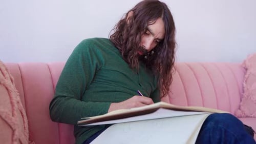 Man Sketching in Notepad on Pink Couch Indoors
