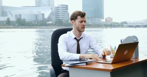 Man Sits in Water Typing on a Laptop Tired From Office