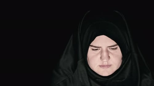 Woman Wearing Dark Head Covering Looks at Camera