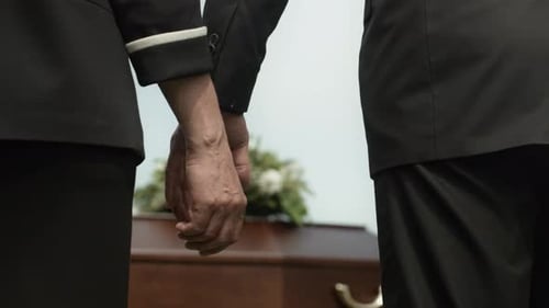 Two Mourners Holding Hands At Funeral