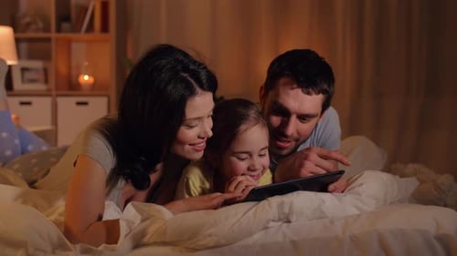 Family fun together using tablet in bedroom at night