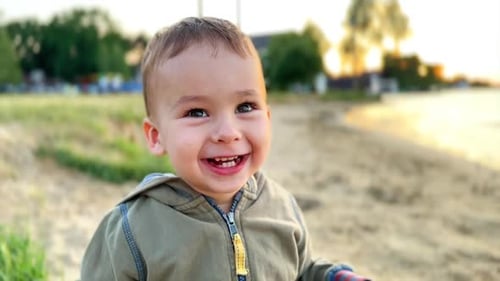 Adorable smiling Caucasian boy on the shore. Curious kid looks into camera. Close up.