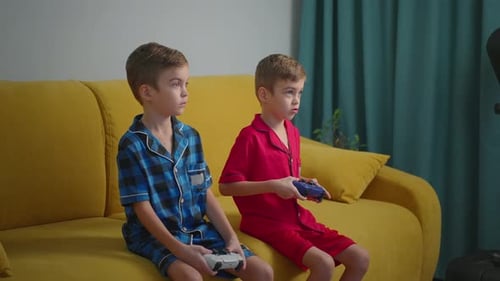 Two Kids Playing Video Games While Sitting on a Yellow Couch Together