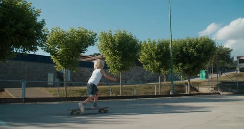 Child Boy Learning to Ride on Long Skate Board at Sport Place on Summer Day