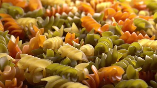 Multicolored italian pasta Fusilli or Rotini rotating in close up background sun light side view