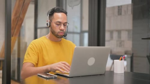 Creative Mixed Race Man with Headset Working on Laptop in Call Center