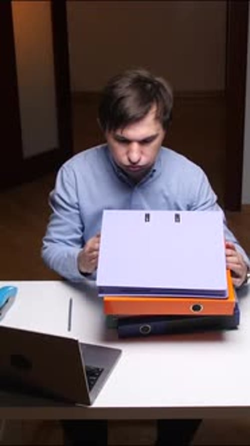 Vertical Video Office Worker Looking Stressed at Binders Sitting at Desk