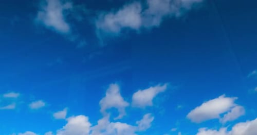 Blue summer sky with little soft white clouds floating quickly. Low angle view. Timelapse.