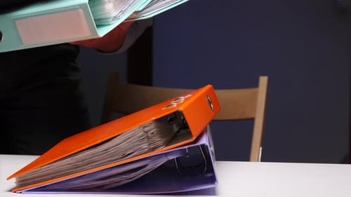 Person Carrying Stack of Heavy Office Binders Full of Paperwork