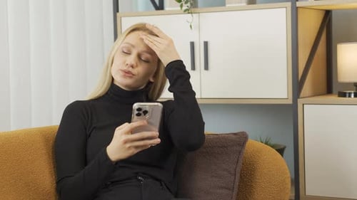 Woman on Couch Using Phone with Frustration