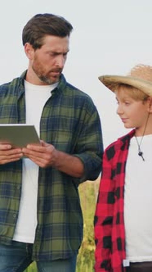 Father and Son Working on Farm Two Farmers Man and Boy Using Tablet Computer to Manage Ve Getables
