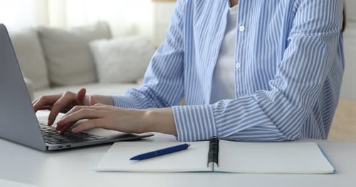 Woman Typing on Laptop and Writing in Notebook