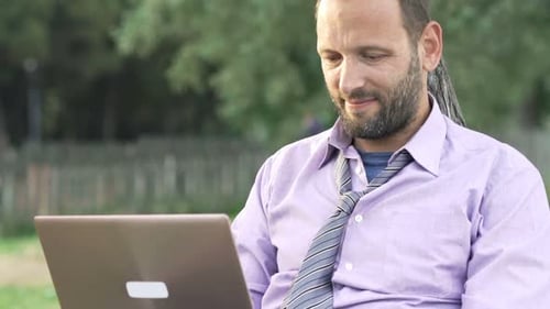 Junger Geschäftsmann arbeitet an einem sonnigen Tag im Freien im grünen Park am Laptop