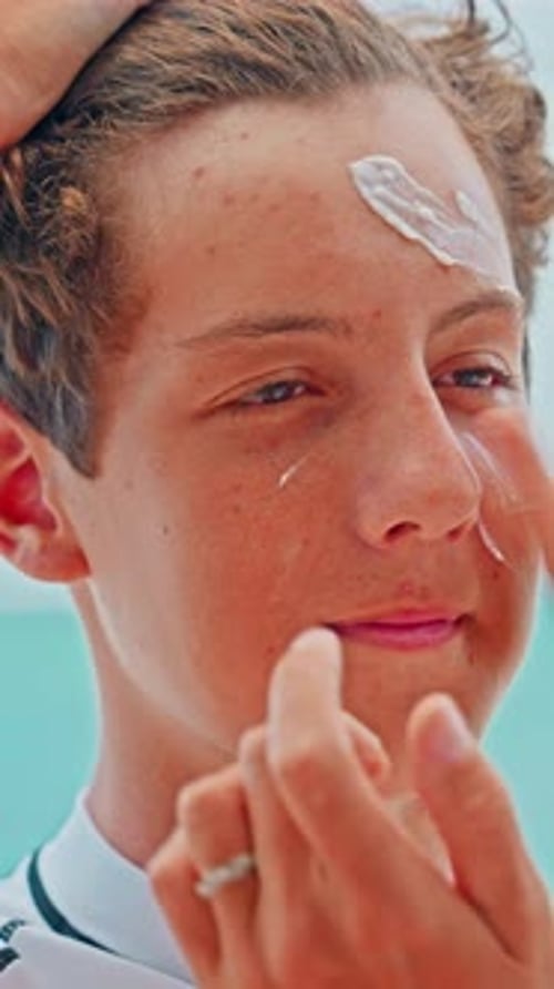 A Mother Applies Sunscreen to Her Teenage Son's Face Against a Beautiful Ocean Backdrop on a